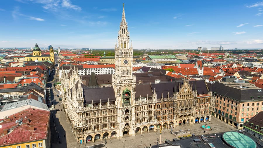 Blick von oben auf das Neue Rathaus in München am Marienplatz mit seiner mächtigen, prachtvollen, neugotischen Fassade und über die Stadt