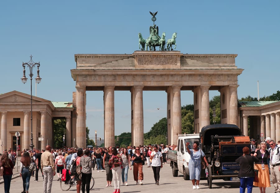 Brandenburger Tor in Berlin, Sonne, blauer Himmel, Blick von Pariser Platz, Quadriga von vorn, viele Menschen vor Brandenburger Tor in Sommerkleidung auf Pariser Platz