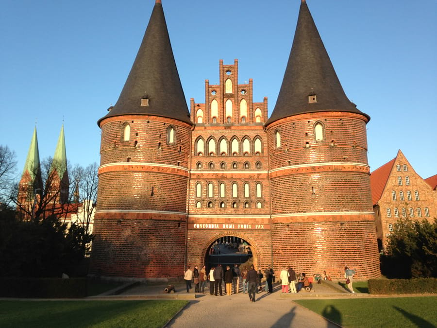 Das Holstentor in Lübeck mit seinen imposanten roten Doppeltürmen und den dicken gotischen Backsteinmauern strahlt in der Sonne mit blauem Himmel.