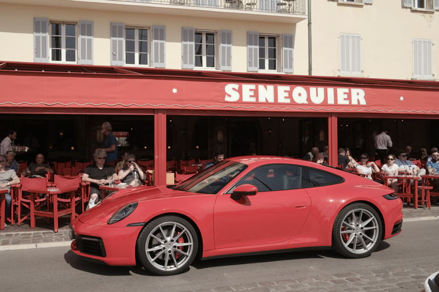 Roter Porsche 911 Carrera S 992 steht vor der berühmten roten SENEQUIER Bar in Saint-Tropez am Hafen.