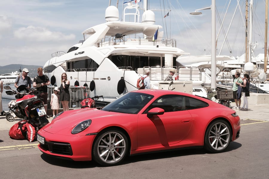 Roter Porsche 911 Carrera S 992 steht vor großer, weißer Luxus-Yacht in Saint-Tropez im Hafen.