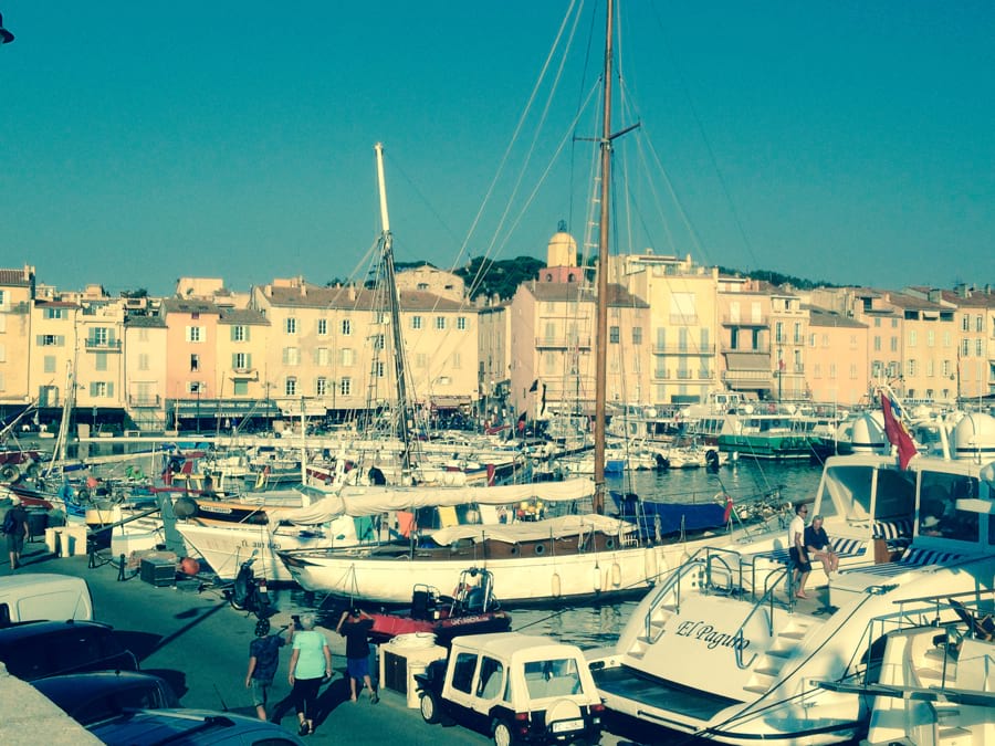 Segelboote und Motor-Yachten liegen im Hafen von Saint-Tropez, dahinter die typischen gelben und orangefarbenen provenzalischen Häuser von Saint-Tropez. Blauer Himmel, Sonne