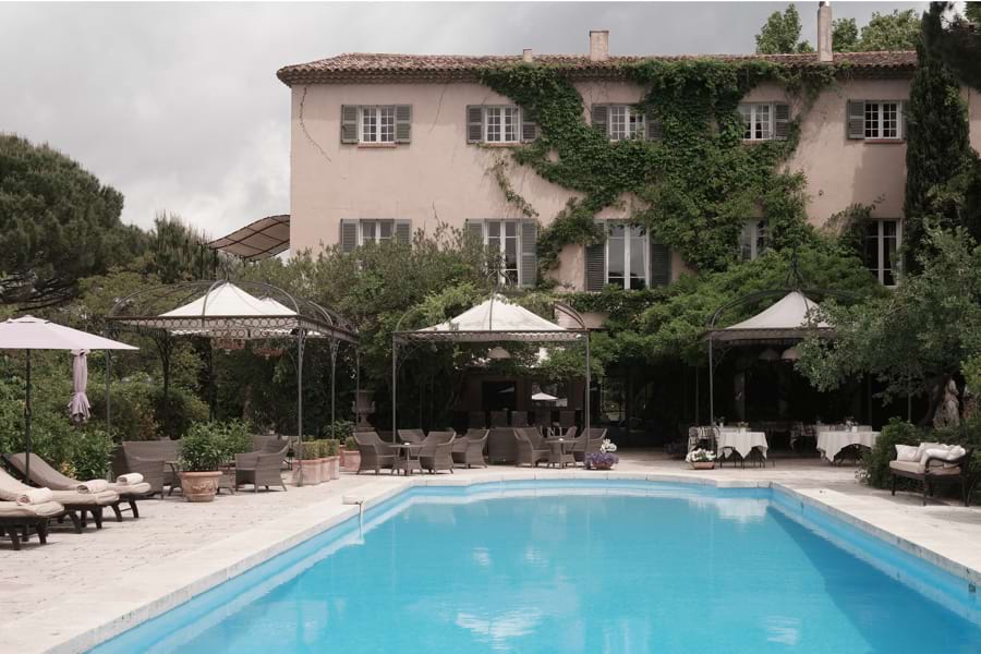 5-Sterne-Luxushotel Mas de Chastelas als Herrenhaus der Provence aus dem 18. Jahrhundert, davor großer Swimming Pool. Das Restaurant auf der Terrasse rechts direkt am großen Pool lädt ein auf der einen Seite, die Außen-Bar auf der Terrasse links mit bequemen Sesseln und Sofas aus Korbgeflecht neben dem Pool auf der anderen Seite. Baldachine spenden Schatten.