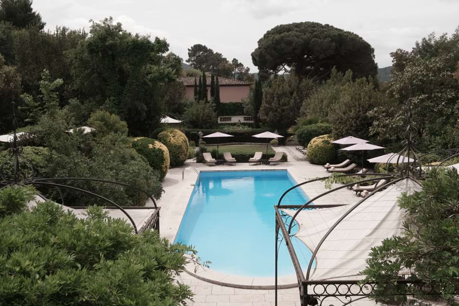 Großer Swimming-Pool mit Liegen und Sonnenschirmen in einem wunderschönen, mediterranen Park mit grünen Bäumen und grünen Büschen am Luxushotel Mas de Chastelas