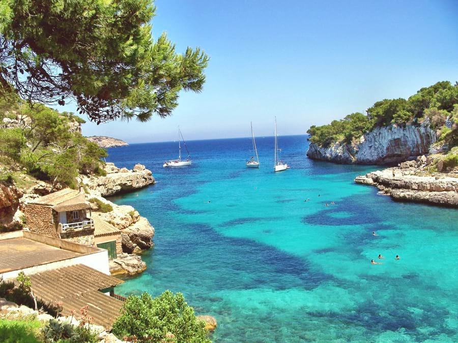 Mallorca Küste türkisblaugrünes Meer malerische Bucht felsige Klippen grüne Bäume grüne Büsche Sonne blauer Himmel