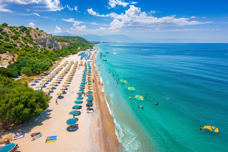 Antalya, Türkische Riviera. Breiter, kilometerlanger, gelbweißer Strand am türkisblauen, kristallklaren Meer. Viele Sonnenliegen und Sonnenschirme für entspannenden Strandurlaub. Urlauber baden im Meer.