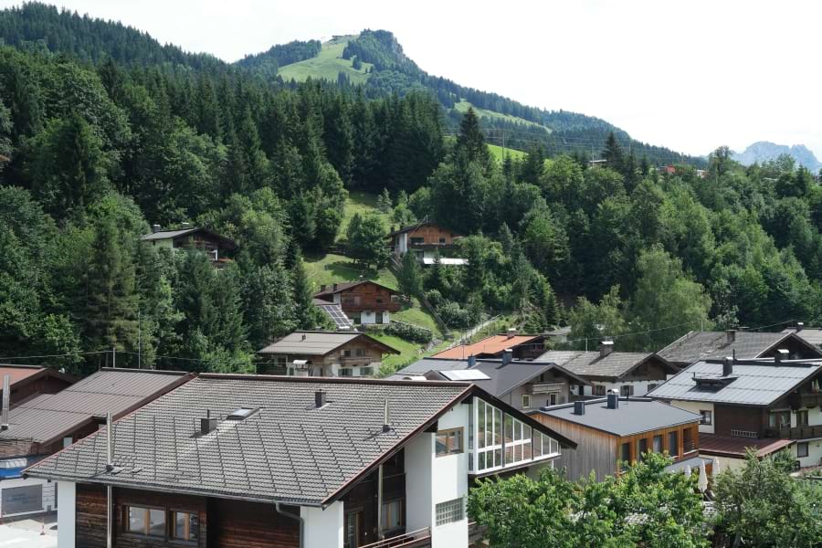 Blick über Häuser auf die herrlichen, umliegenden Berge mit vielen, grünen Nadelbäumen