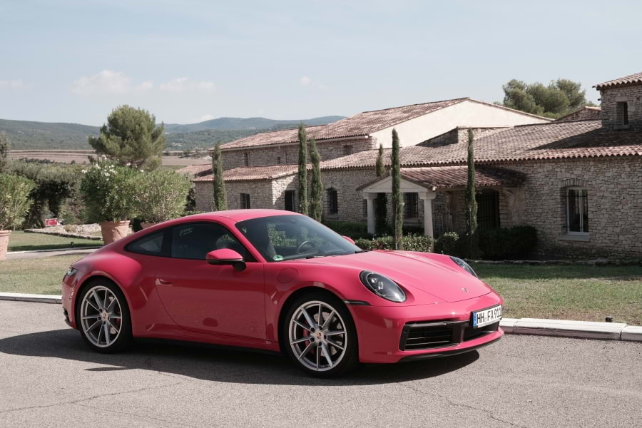 Roter Porsche 911 Carrera S 992 steht vor dem 5-Sterne-Luxushotel Le Phébus & Spa vor dem Eingangsbereich. Hotel Le Phébus & Spa in roher, charakteristischer Architektur aus hellen Trockensteinen im Baustil der Provence. Blauer Himmel, die Sonne scheint.